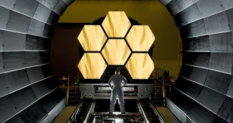 Ein Mann steht vor Spiegelsegmenten des James Webb-Teleskops.