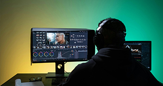 Un hombre sentado frente a una computadora, editando un video
